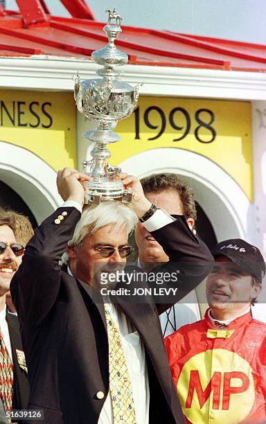 Jockey Kent Desormeaux watches as trainer Bob Baffert places the Woodlawn Vase on his head in the winner's circle after their horse Real Quiet won...
