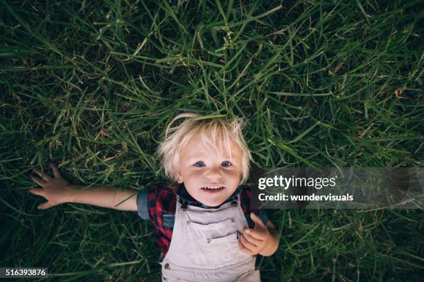 cute blonde child lying on the grass - playful portrait stock pictures, royalty-free photos & images