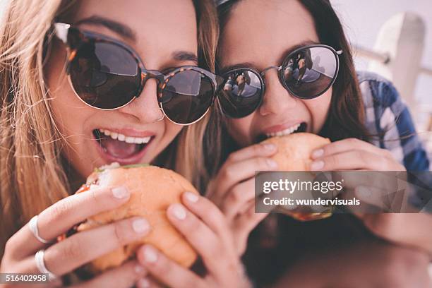 retro style shot of teenage girl best friends eating burgers - burgers stockfoto's en -beelden
