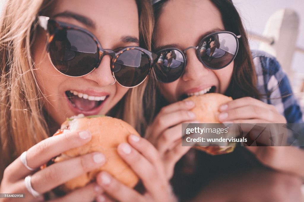 Retro style shot of teenage girl best friends eating burgers