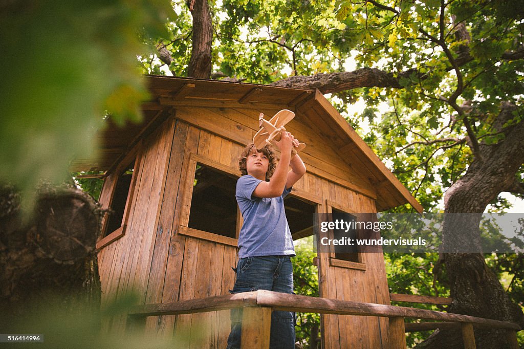 Boy in a treehouse daydreaming with his toy wooden plane
