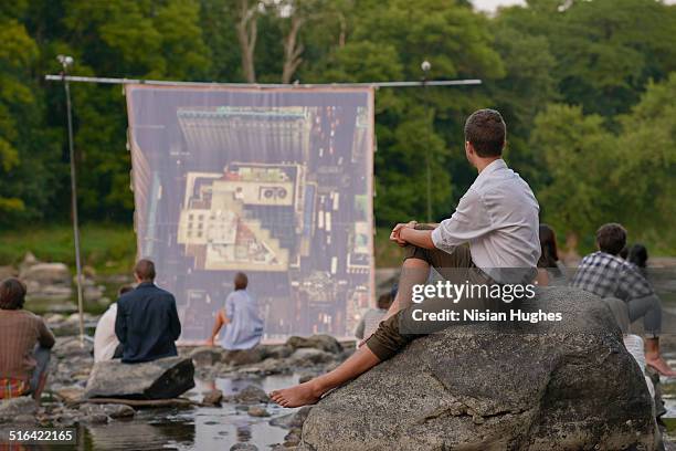 people on river sitting in front of movie screen - open air kino stock-fotos und bilder