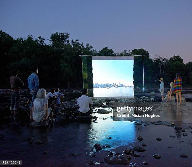 people on river watching movie screen - beamern stock-fotos und bilder