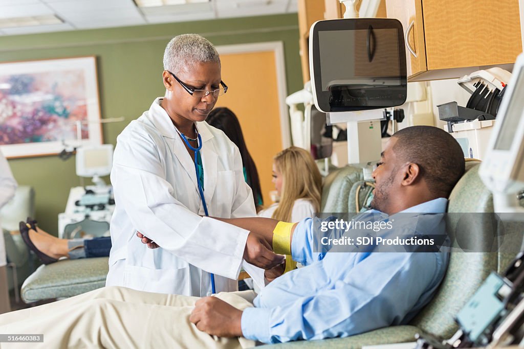 Senior phlebotomist bandaging patient's arm after he gives blood