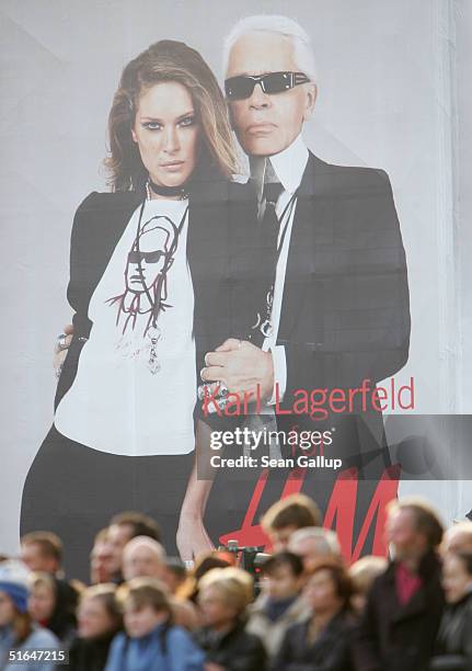 People await the arrival of British Queen Elizabeth II near a giant 1,500 square meter advertisement for Swedish fashion retailer H&M that shows...