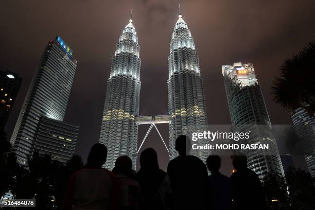 People stand in front of Malaysia's landmark Petronas Twin Towers before the lights had been switched off during the Earth Hour campaign in Kuala...