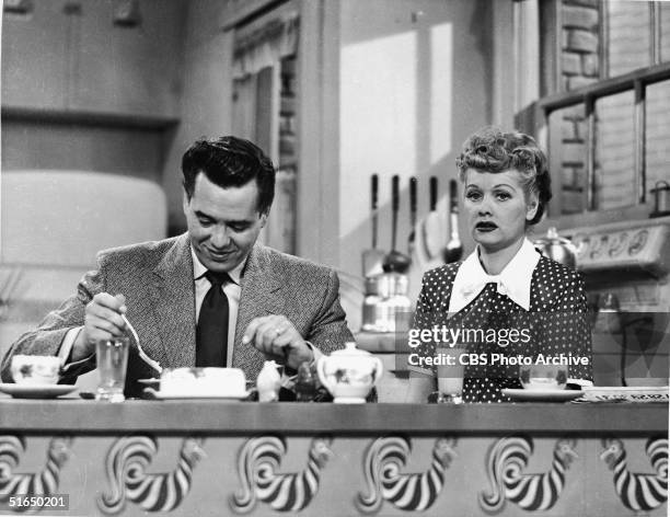 Cuban-born actor Desi Arnaz sits at the kitchen table and eats breakfast alongside his real-life wife American actress and comedienne Lucille Ball in...