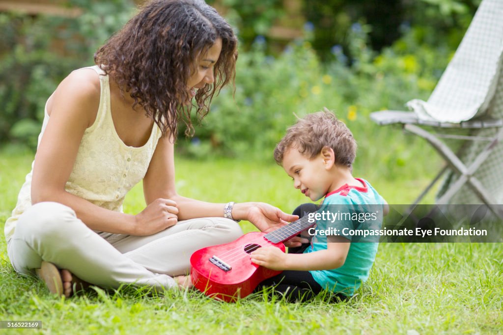 Child playing ukelele in garden with mother