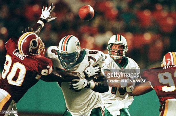 Miami Dolphins' quarter back Dan Marino passes through the defense of Washington Redskins' defensive ends Kenard Lang and Chris Mimms with help of...