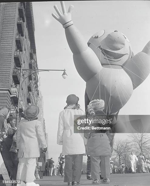 New York: Photo shows kids in foreground looking on as one of the big balloons in the Macy Parade passes them...