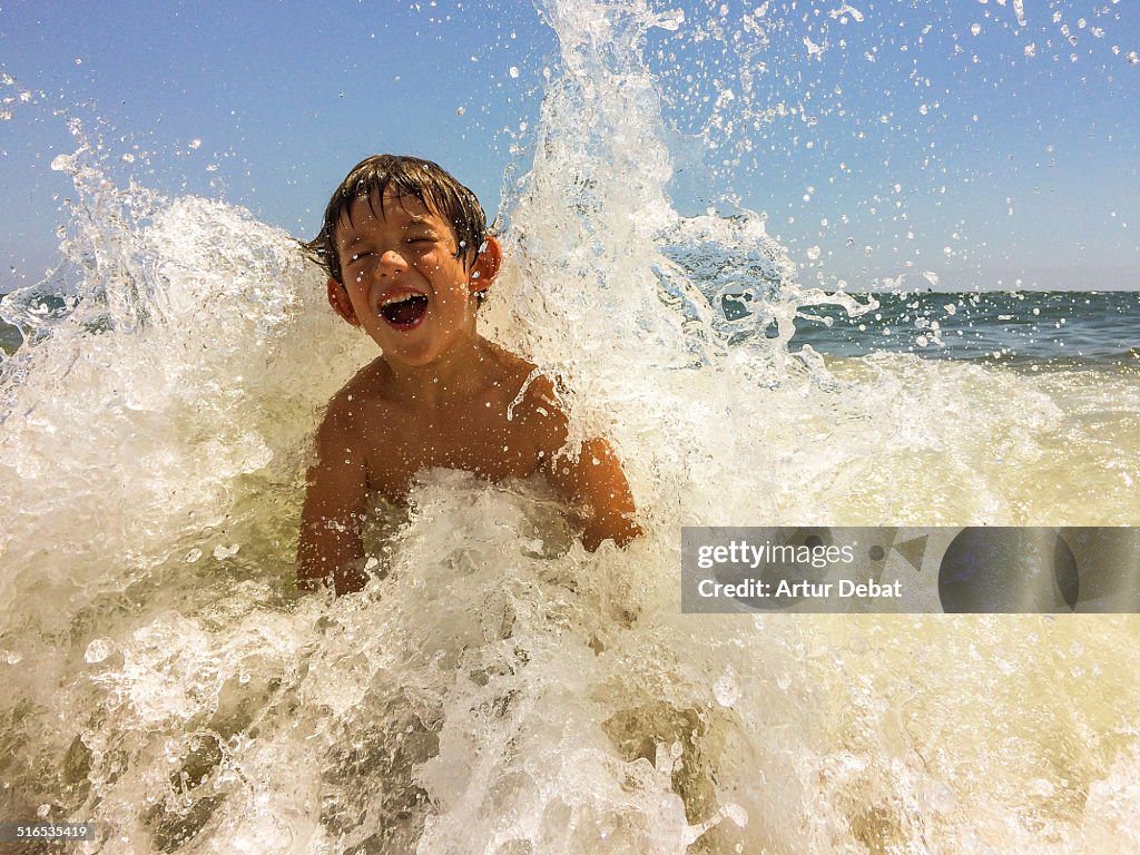 Kid get splashed by wave in beach on summertime.