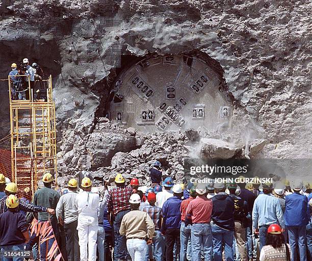 Workers watch as a Department of Energy tunnel boring machine emerges after it bore a 25 foot diameter, 5 mile long horseshoe shaped tunnel through...