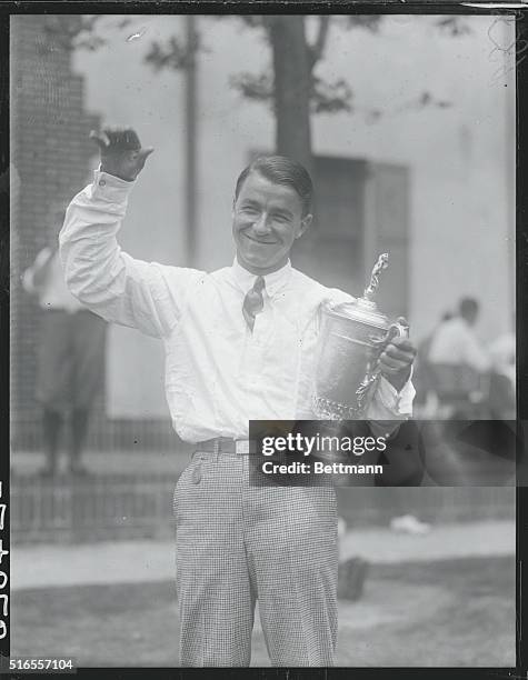 Golfer Gene Sarazen is shoen here as he waves while holding his trophy.