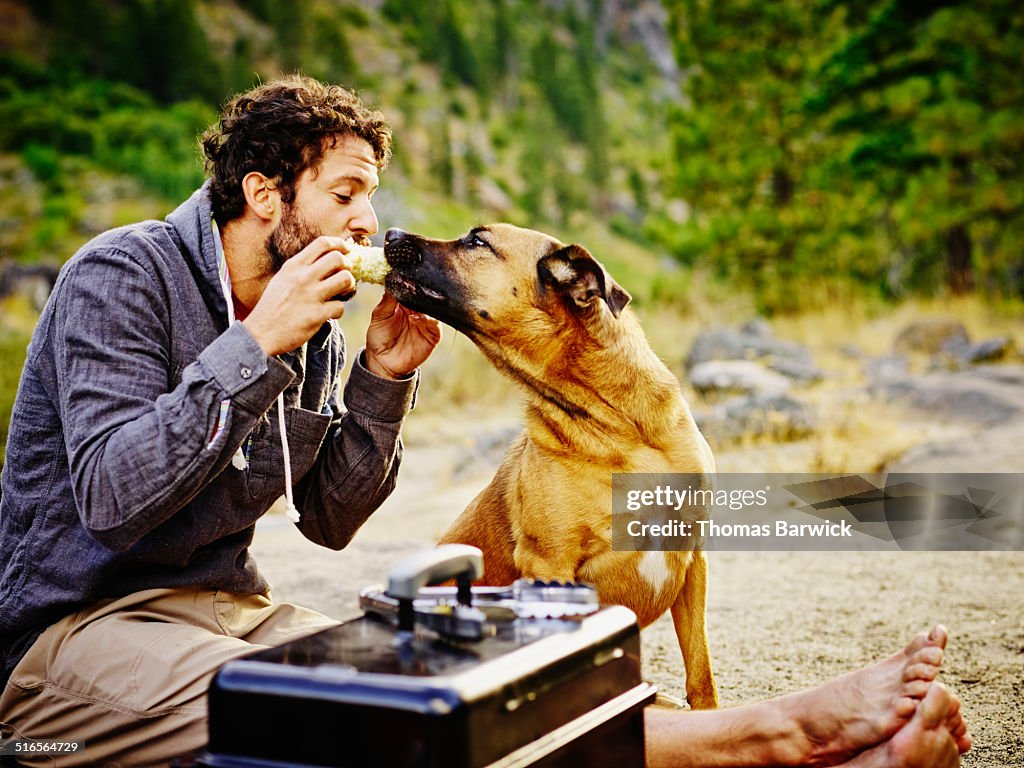 Man sharing corn on the cob with dog while camping