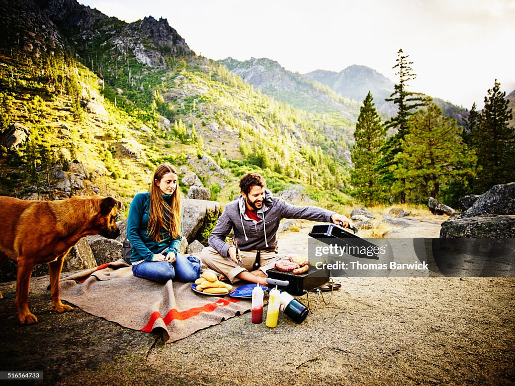 Couple camping with dog barbecuing at sunset