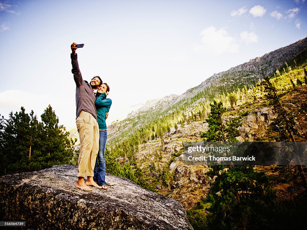 Smiling couple on boulder taking self portrait