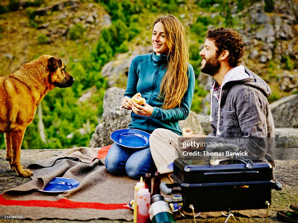 Smiling couple with dog grilling and eating dinner