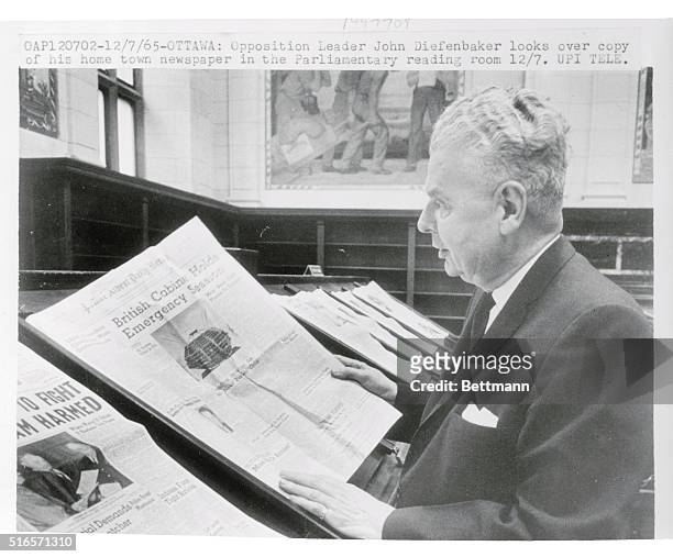 Ottawa: Opposition Leader John Diefenbaker looks over copy of his home town newspaper in the Parliamentary reading room.