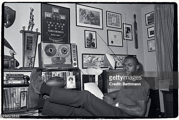 Gale Sayers, rookie star of the Chicago Bears, relaxes in the trophy room of his home here recently. Sayers six touchdowns in the December 12th game...