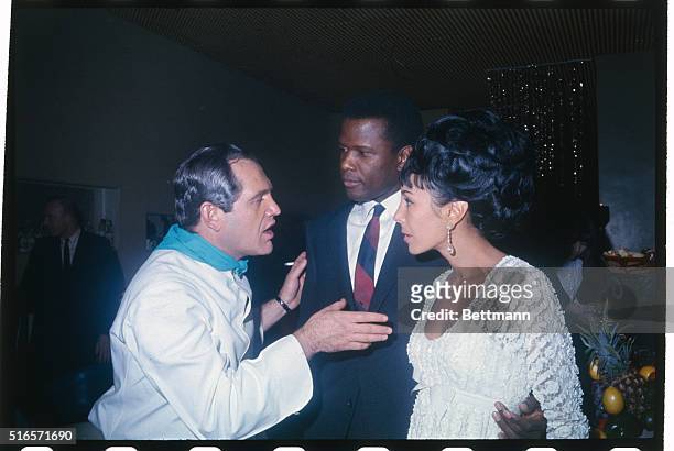 Comedian Alan King visits with Sidney Poitier and Mrs. Harry Belafonte who were guests at a party which King hosted February 10 at La Fonda Del Sol...