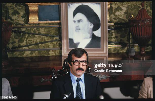 Sitting under the Khomeini's portrait, Iranian presidential spokesman, Bani Sadr Moudadi Garmarodi, protests the arrest and deportation of Iranians...