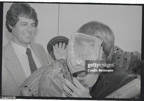 Phillies' star Bob Boone watches as teammate Pete Rose peers through a see-through fielders glove as they check out some baseball equipment of the...