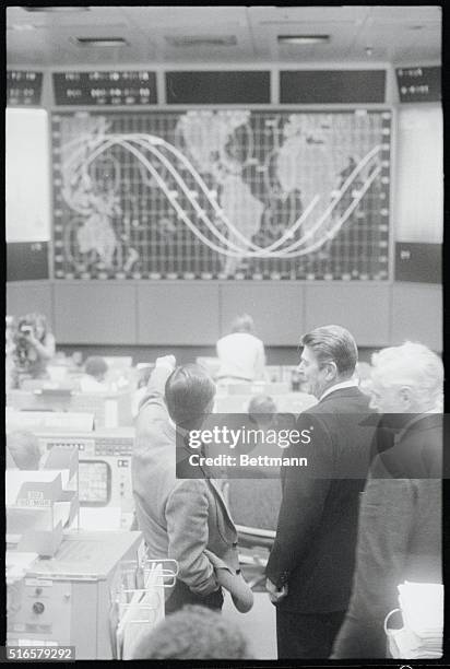 Johnson Space Center Director Christopher Kraft Jr. Points to the orbit tracking map in Mission Control, telling President Reagan the current...