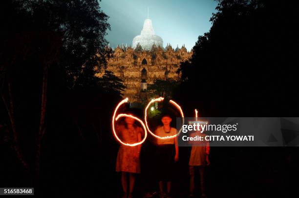 This picture taken in Magelang, Central Java on March 19, 2016 shows Indonesian activists holding candles featuring 60+ as Budhist temple Borobudur...