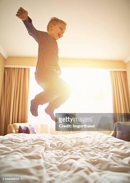 little boy mid air jumping with joy on bed. - a boy jumping on a bed stock pictures, royalty-free photos & images