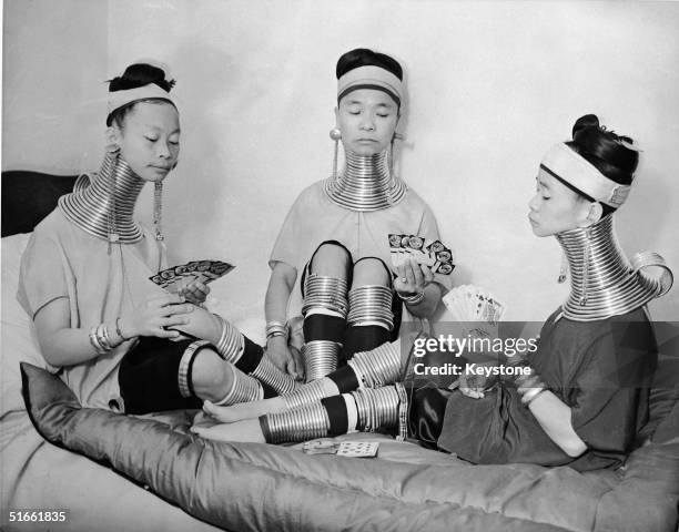 Three Burmese women members of a circus play cards as they wear the brass neck and leg rings traditionally worn by Padaung women since childhood and...