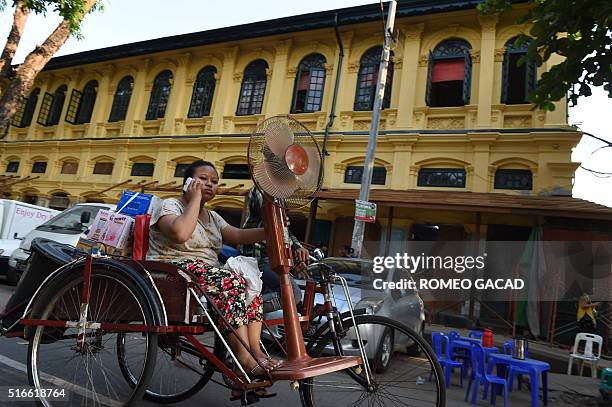In this photograph taken on March 19 a Myanmar woman transports an electric fan and other items on a trishaw in Yangon as the month of March starts...