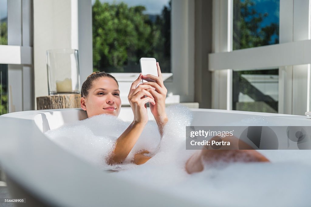 Beautiful woman using smart phone in bathtub