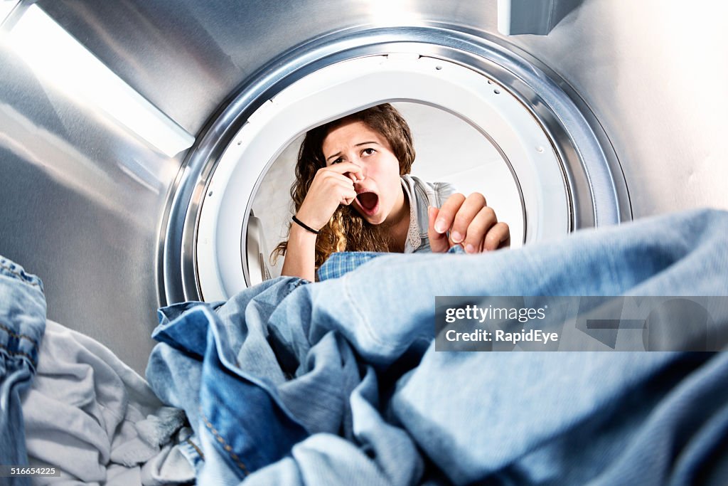 Laundry left in clothes dryer stinks! Unhappy woman holds nose.