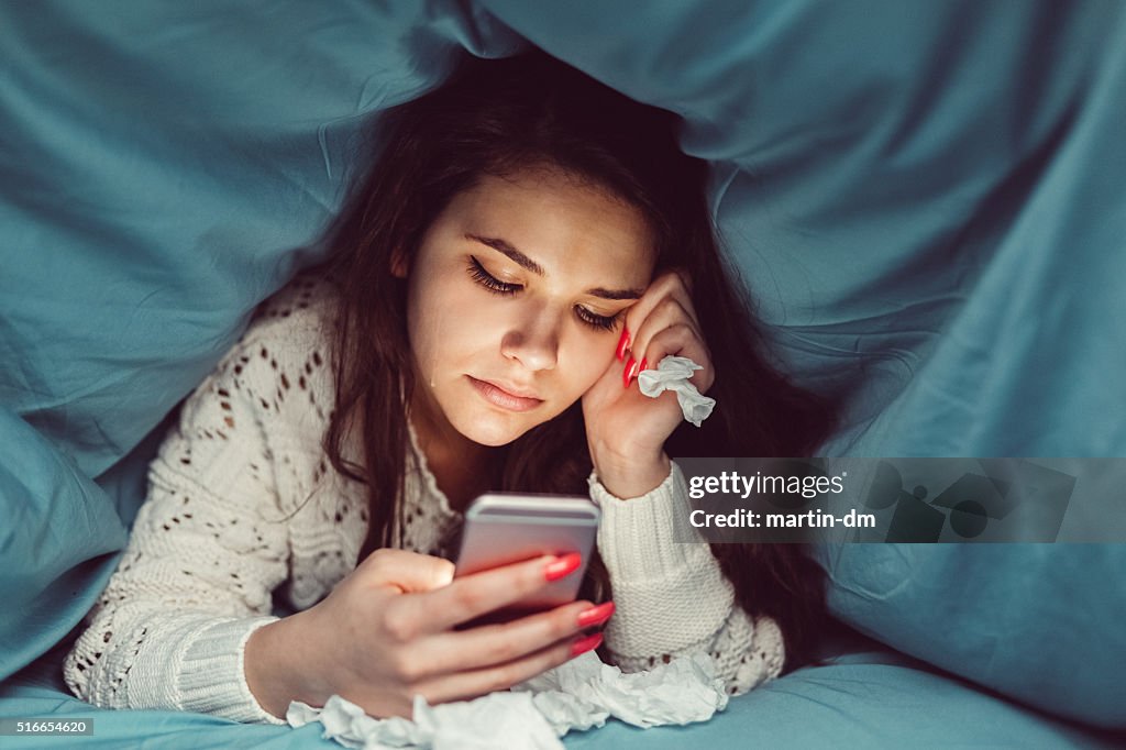 Crying girl in bed texting on smartphone