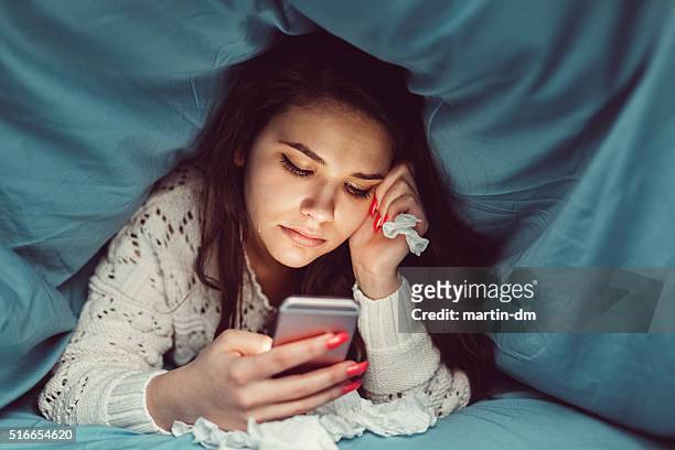 crying girl in bed texting on smartphone - relationship difficulties stock pictures, royalty-free photos & images