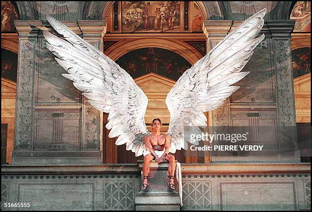 Model with bare torso and giant Icarus feather wings looks down from the first floor balcony of the high-ceilinged hall in the Ecole des Beaux-Arts...