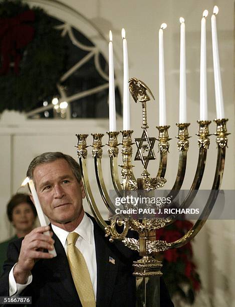President George W. Bush raises a lit candle to the White House menorah on the 6th night of Hanukkah 04 December 2002 during ceremonies at the White...