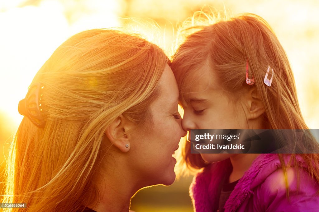 Mother and daughter kissing at sunset closeup