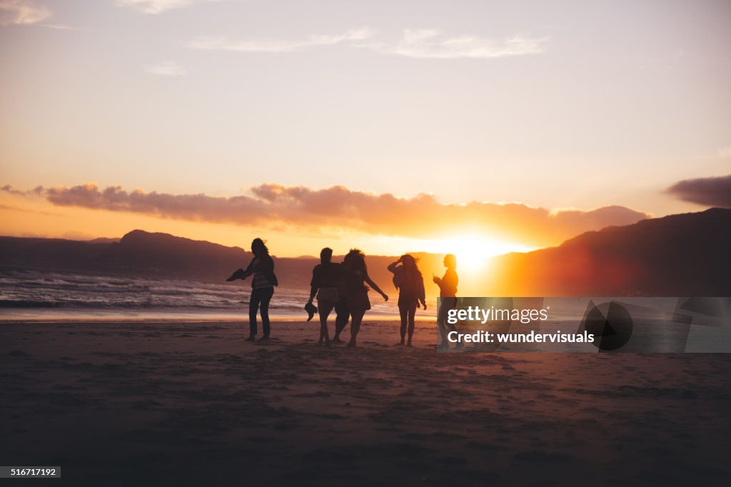 Silhouette of teen friends dancing on the beach at sunset