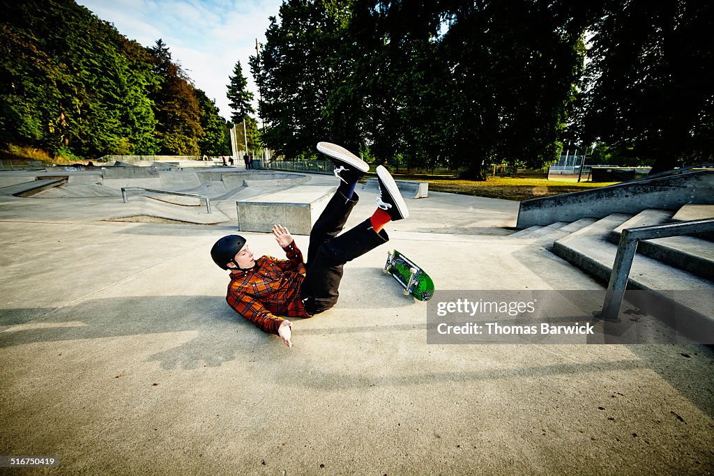 Skateboarder falling off of railing in skate park