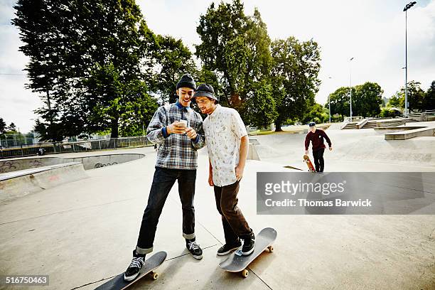 two smiling skateboarders looking at smartphone - friends skating stock pictures, royalty-free photos & images