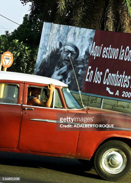 An old American car passes 19 April 2001 in front of a poster referring to the 40th anniversary of the Cuban armed forces victory, in Playa Giron,...