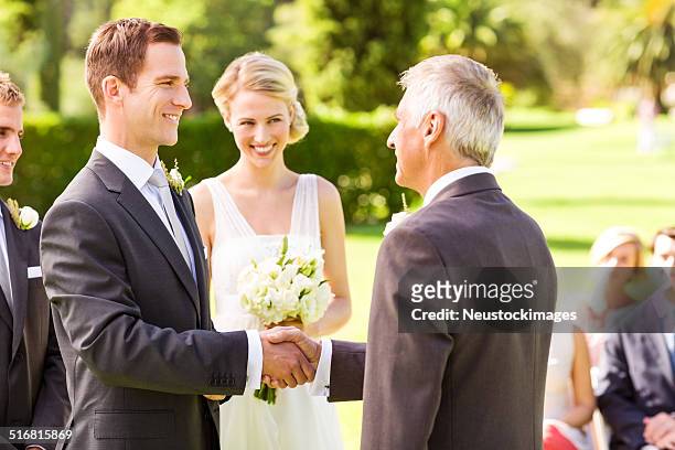 bräutigam beim händeschütteln mit vater im garten - bride father stock-fotos und bilder