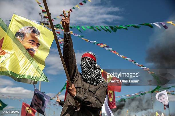 Kurdish man wearing a mask flashes the v-sign as he holds up a flag with a picture of the jailed PKK leader Abdullah Ocalan during Newroz...