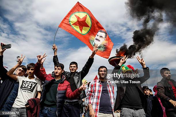 Kurdish men flash v-signs as they hold up a flag with a picture of the jailed PKK leader Abdullah Ocalan during Newroz celebrations, on March 21,...