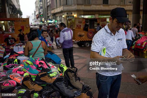 Man pays for shoes he purchased at an outdoor market in Medellin, Colombia, on Monday, March 14, 2016. Colombia's central bank raised its benchmark...
