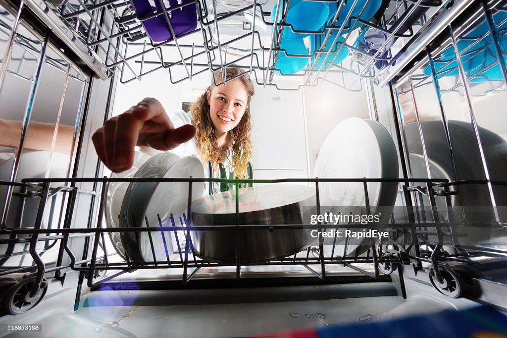 Seen from inside dishwasher, cute smiling girl loading or unloading