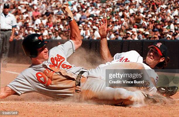 Brady Anderson of the Baltimore Orioles slides safely across home plate ahead of throw to pitcher Mike James of the California Angels on a wild pitch...