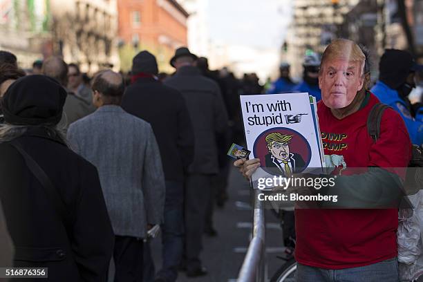 Protester holds a sign and wears a mask in the likeness of Donald Trump, president and chief executive of Trump Organization Inc. And 2016 Republican...