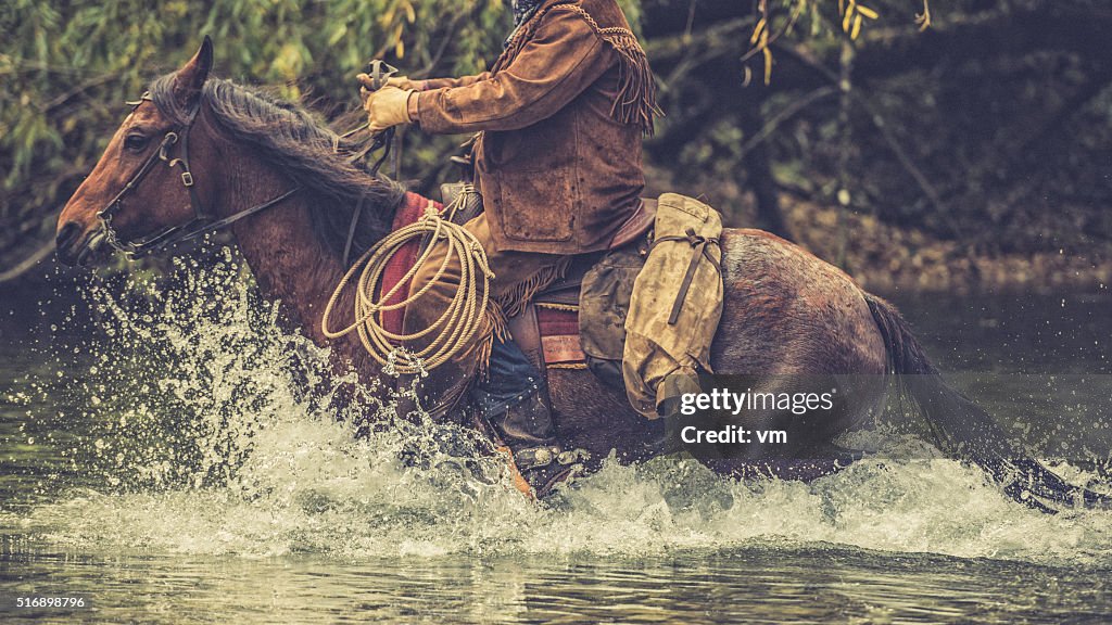 Cowboy su passeggiate un cavallo attraverso un fiume